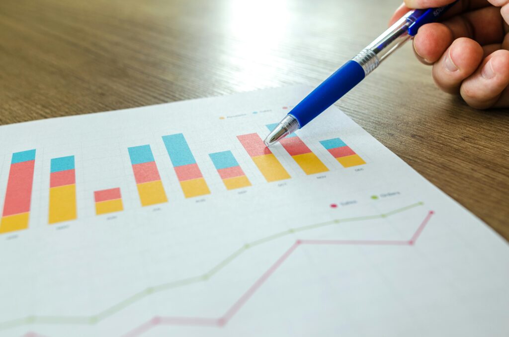 pexels photo 590020 590020 Detailed close-up of a hand pointing at colorful charts with a blue pen on wooden surface.